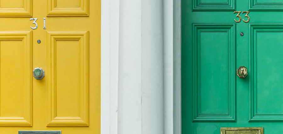 Two doors, one yellow, one green, stand closed side by side. They have brass doorknobs set in the middle, have brass letter slots, and are numbered 31 and 33 respectively.