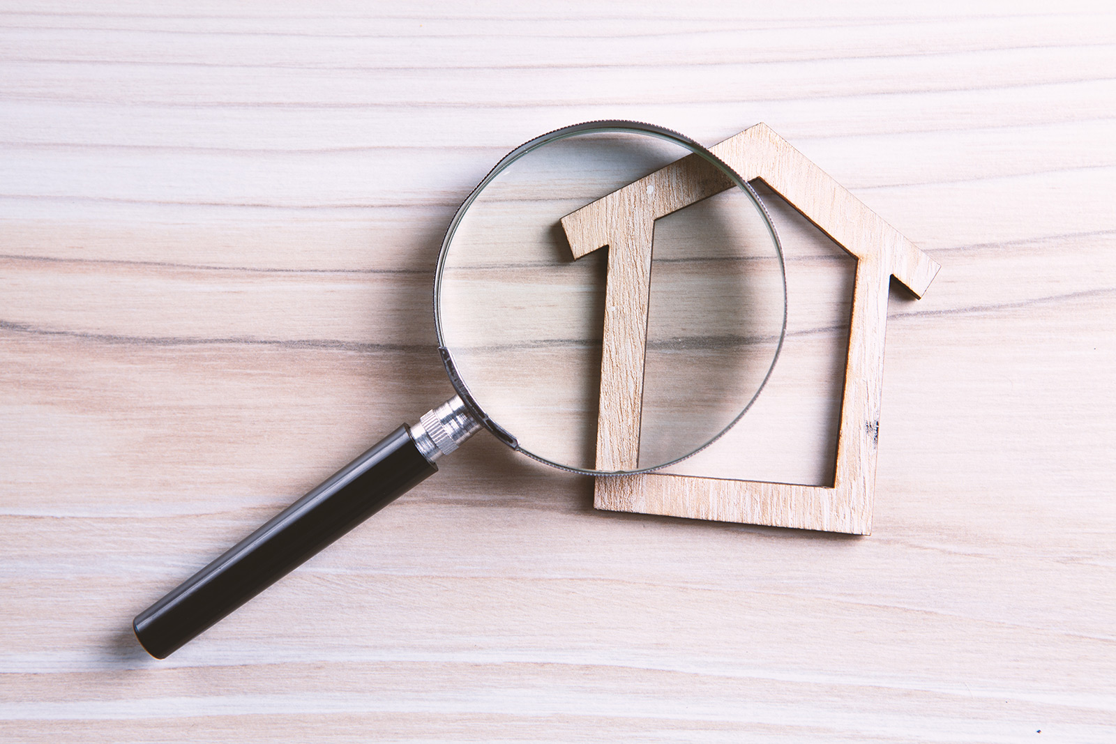 A magnifying glass rests on top of a wooden house figure, sitting on a cedar background.